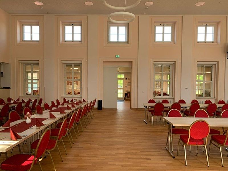 Großer Festsaal, mit braunen Parkettboden, Bankettbestuhlung mit Stühle mit rotem Bezug, hohe Decken und gute Helligkeit im Raum