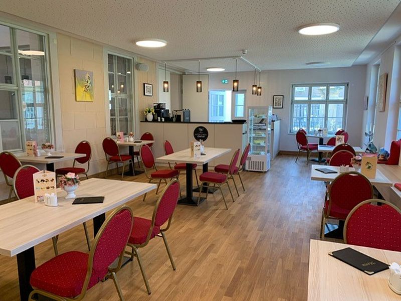 Café Innenansicht, mit braunen Parkettboden, Bankettstühle mit rotem Bezug, Tresen und Kuchentheke