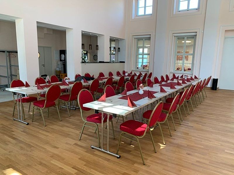 Großer Festsaal, mit braunen Parkettboden, Bankettbestuhlung mit Stühle mit rotem Bezug, hohe Decken und gute Helligkeit im Raum