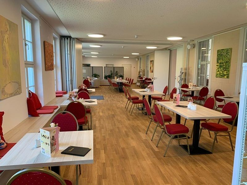 Café Innenansicht, mit braunen Parkettboden, Bankettstühle mit rotem Bezug, helle Räumlichkeiten mit viel Licht und Platz