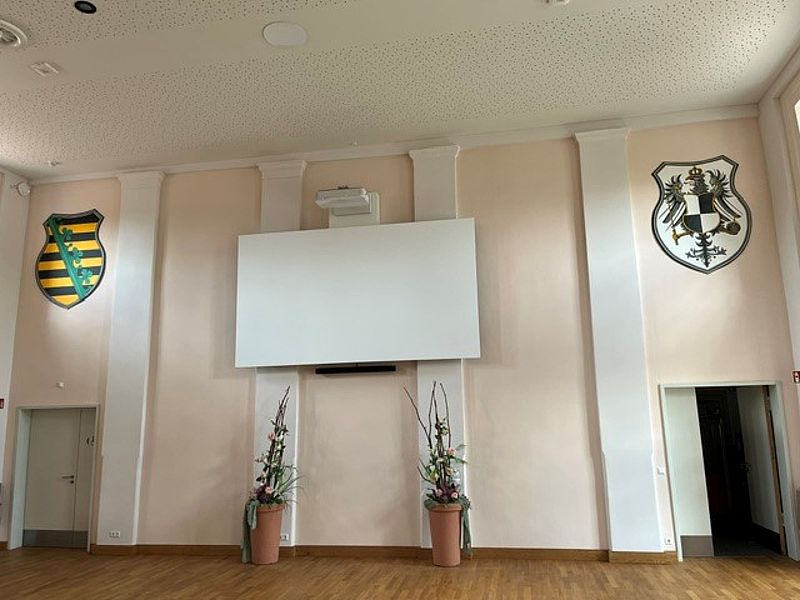 Großer Festsaal, mit braunen Parkettboden, Beamer und eine große Leinwand, hohe Decken und gute Helligkeit im Raum