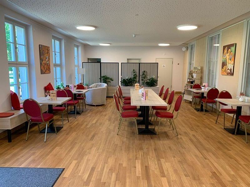Café Innenansicht, mit braunen Parkettboden, Bankettstühle mit rotem Bezug, Eingangsbereich
