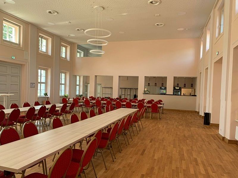 Großer Festsaal, mit braunen Parkettboden, Bankettbestuhlung mit Stühle mit rotem Bezug, hohe Decken und gute Helligkeit im Raum